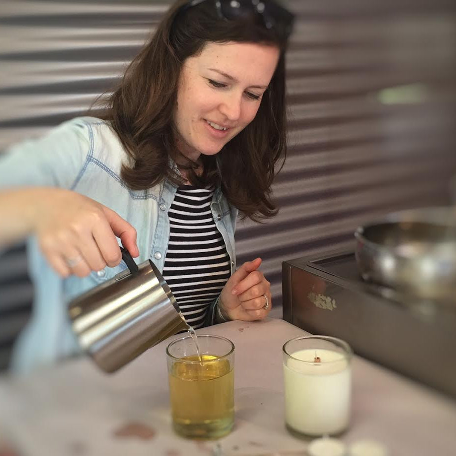 Woman pouring liquid from a silver pitcher into two glasses on a kitchen counter.
